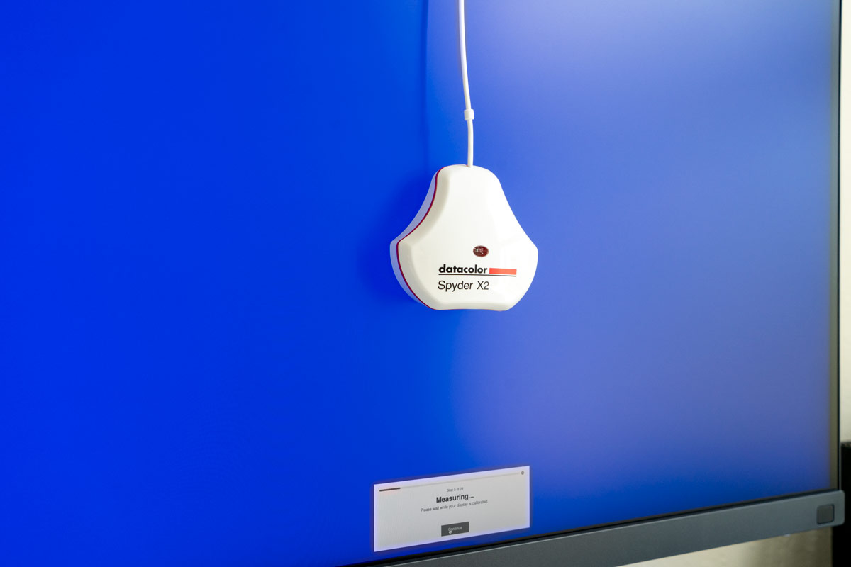 The Datacolor Spyder X2 Ultra monitor calibration tool hangs on a monitor with a blue screen displayed during calibration.